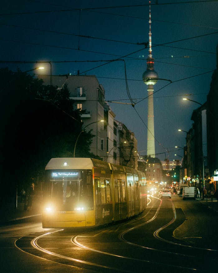 Illuminated Berlin street with tram and Fernsehturm at night.